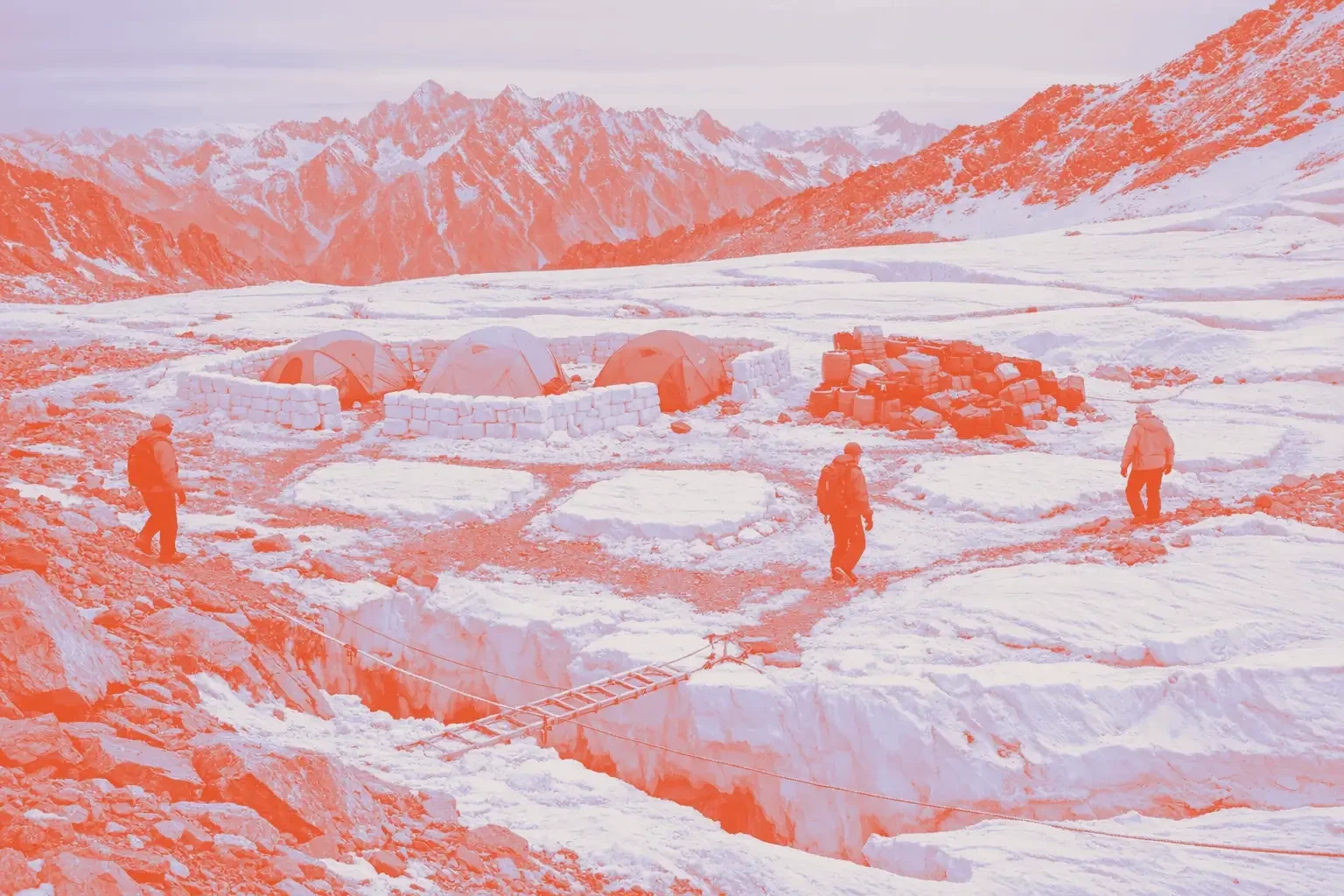 Several tents are set up on snowy terrain with mountains in the background.