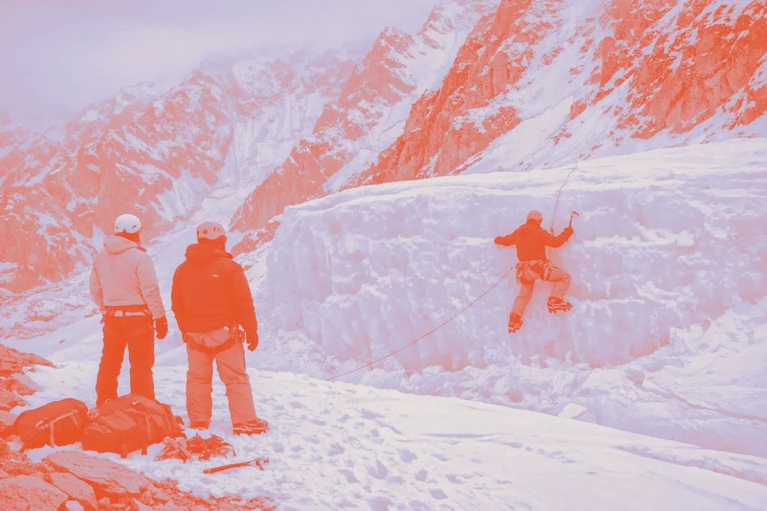 A climber uses ice axes to ascend a frozen wall while two others observe.