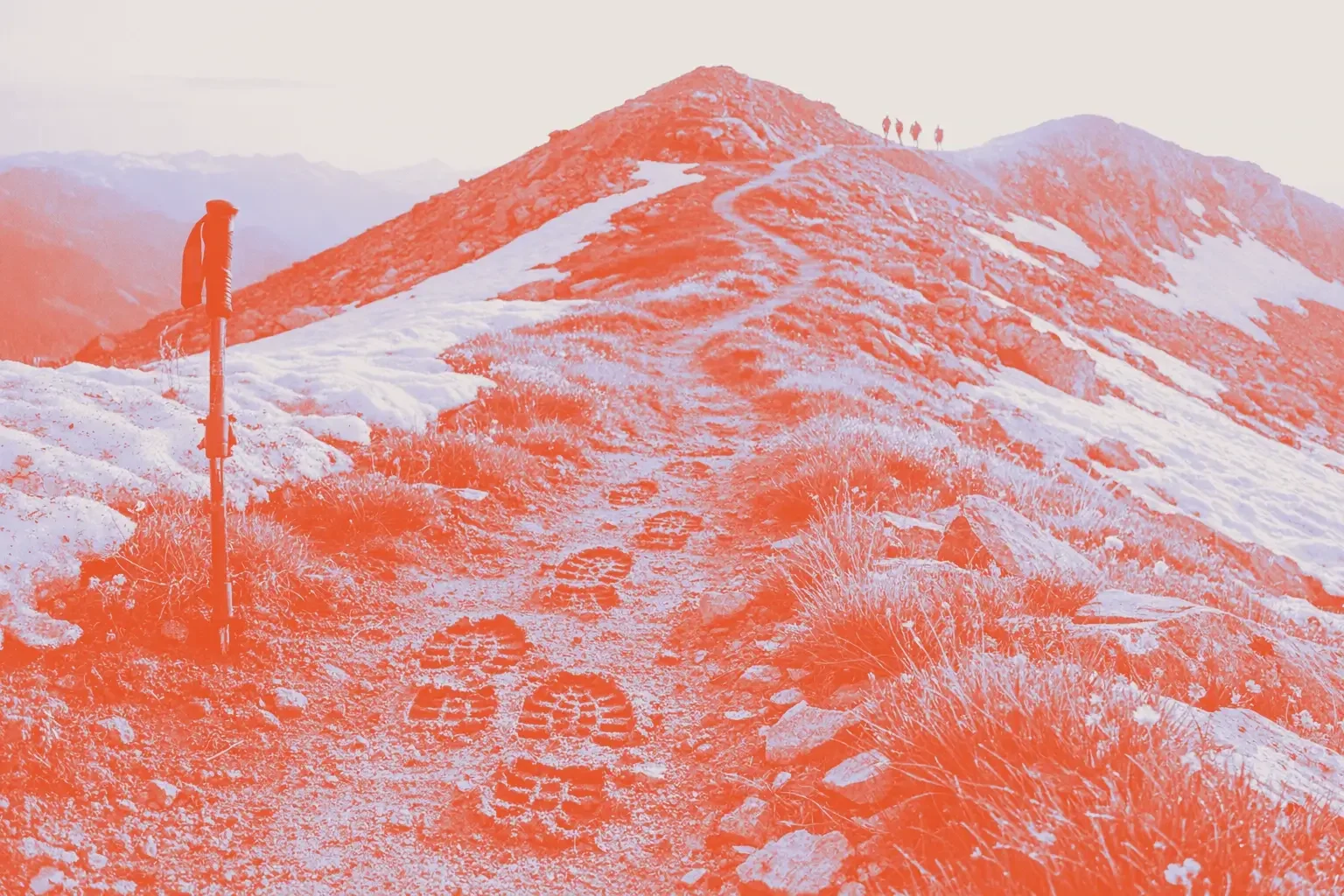A mountain trail with footprints and a trekking pole beside it.
