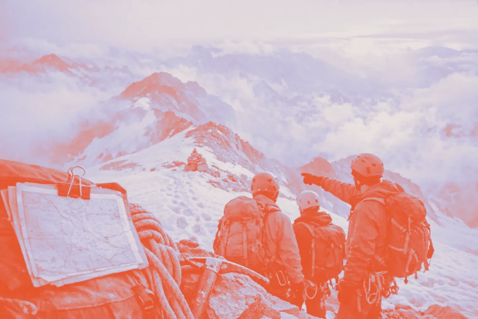 Four mountaineers stand on a snowy peak, looking at a distant mountain range.