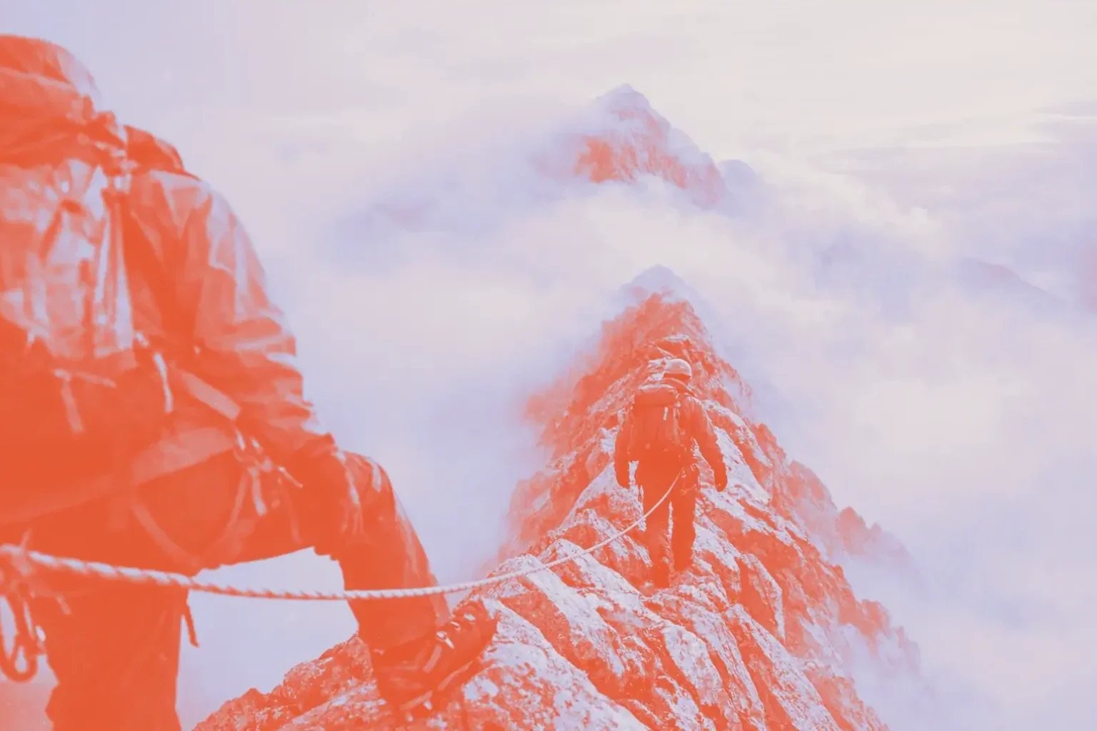 Two climbers walk along a rocky ridge covered in clouds.
