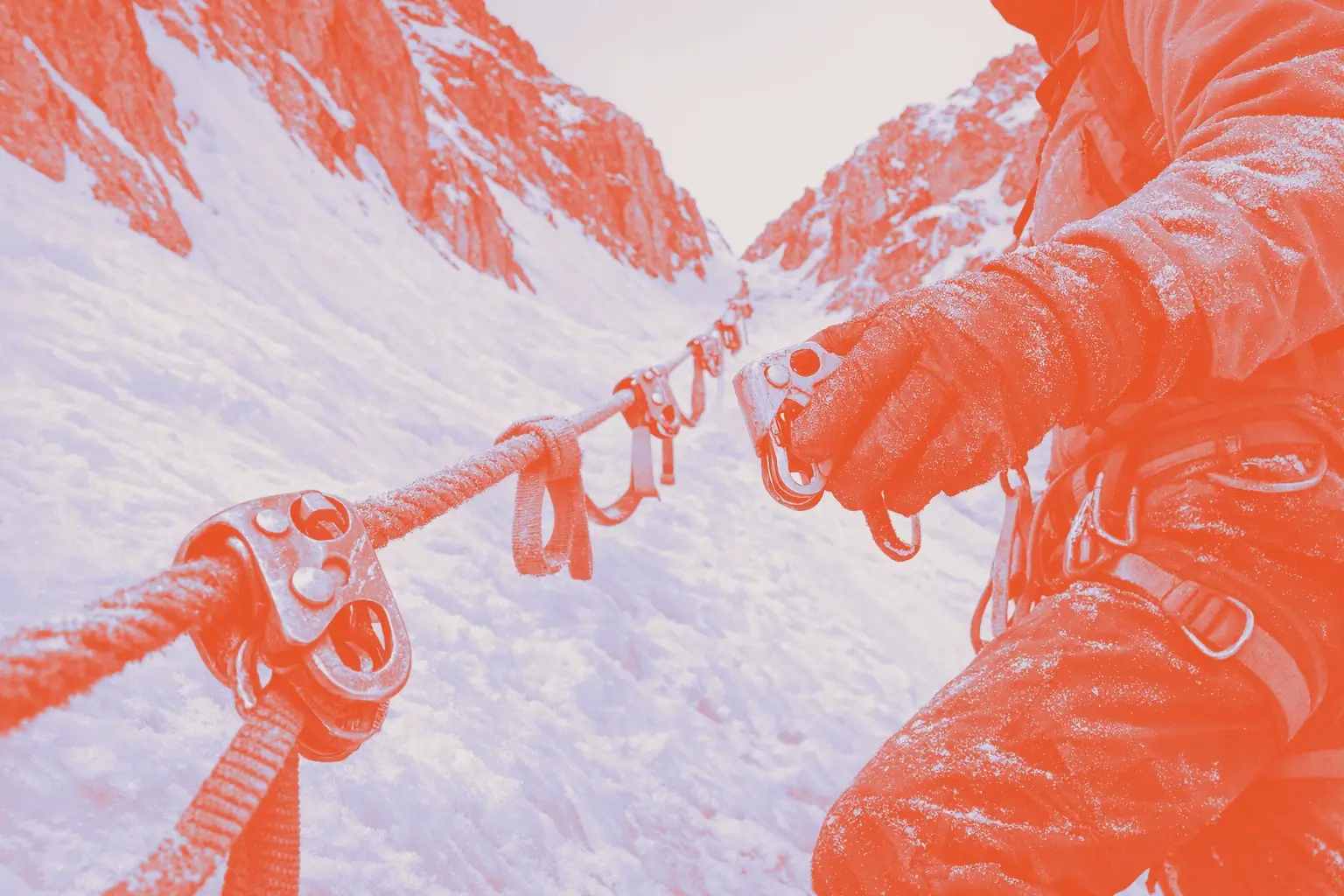 A climber holds a yellow carabiner while standing on a snowy slope, with climbing gear visible on the rope.