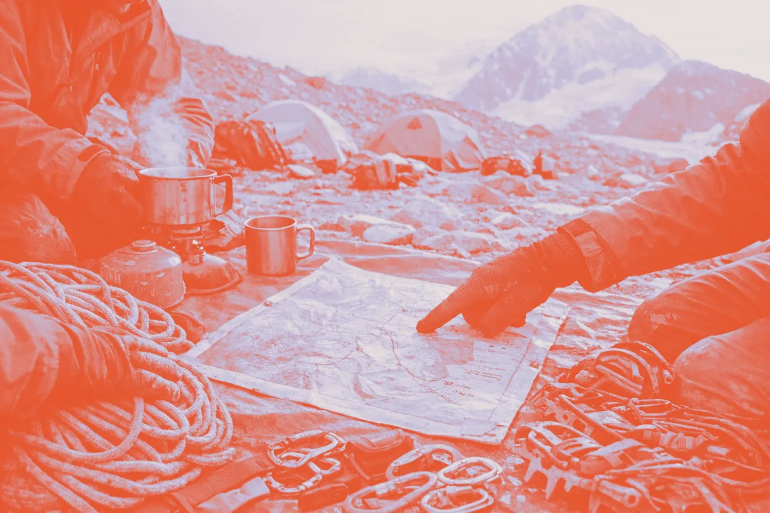 Two climbers are sitting on a rocky surface with a map, cooking equipment, and climbing gear around them.